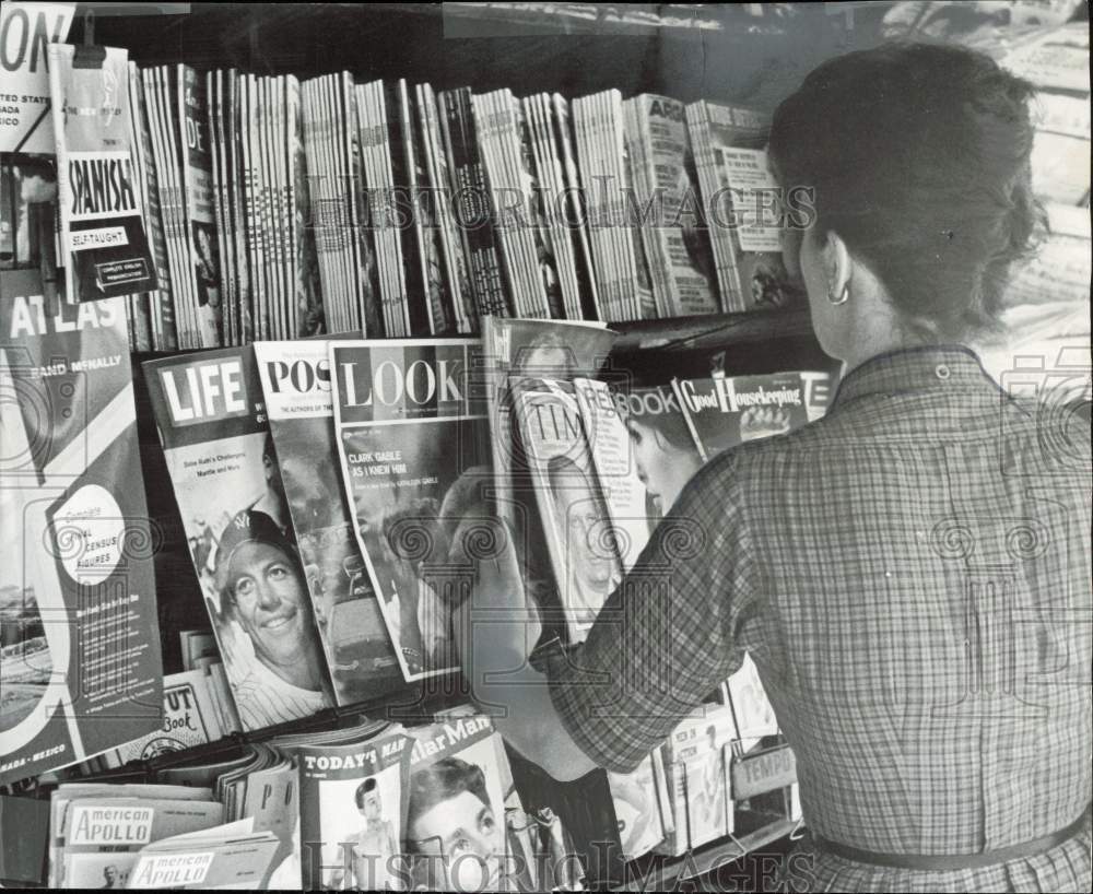 1961 Press Photo Woman checks magazine on a rack at a New York magazine stand